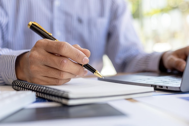 Businessman takes notes in a notebook, owns a startup company, sits in his office and checks the company's financial summary prepared by the finance department. Management concept of startup company.