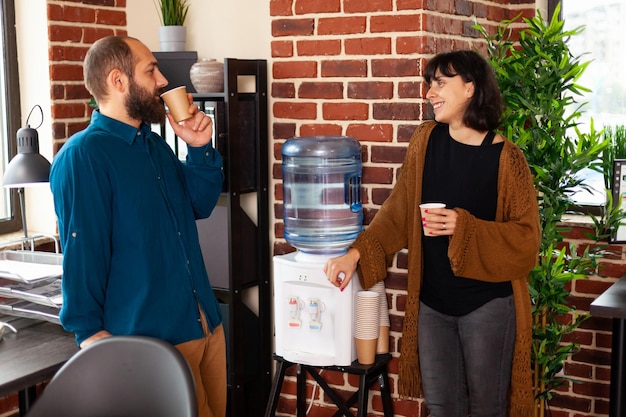 Uomo d'affari che fa una pausa di lavoro parlando con il manager esecutivo che collabora e comunica nell'ufficio di avvio bevendo una tazza d'acqua come rinfresco. uomini d'affari seduti vicino al refrigeratore d'acqua