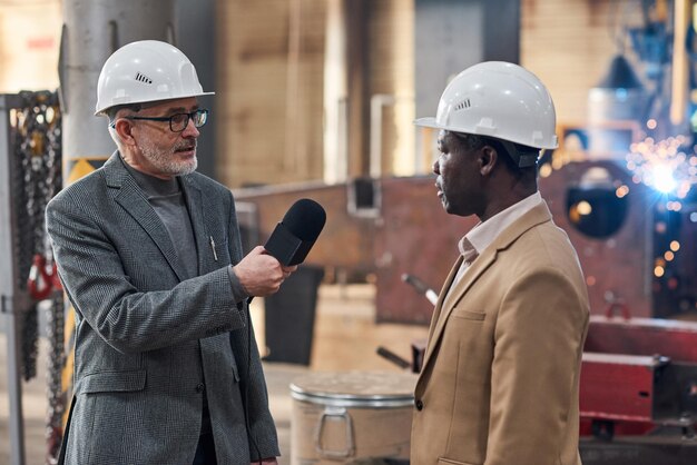 Businessman talking to journalist in factory