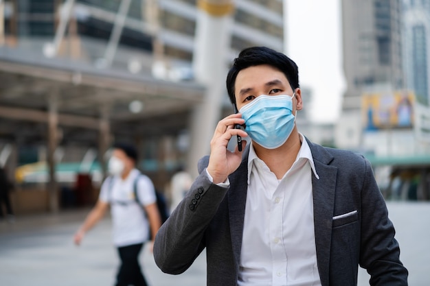 Businessman talking on mobile phone and wearing medical mask during coronavirus pandemic in the city