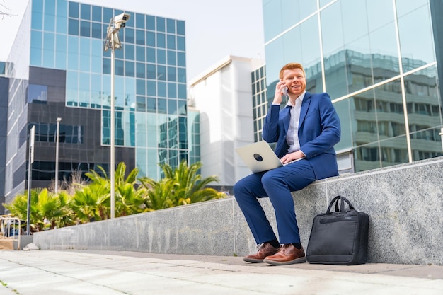 Businessman talking to the mobile while working with laptop in the city