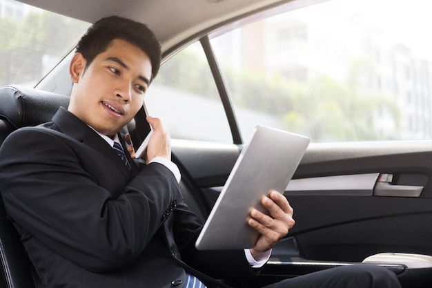 写真 自動車でデジタルタブレットを使用しながら電話で話しているビジネスマン