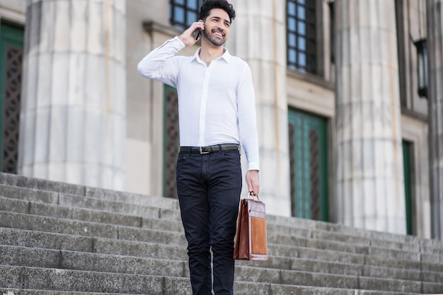 Businessman talking on the phone while standing on stairs outdoors. Business concept.