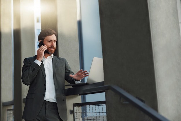 Businessman talking phone with client during break standing near office building