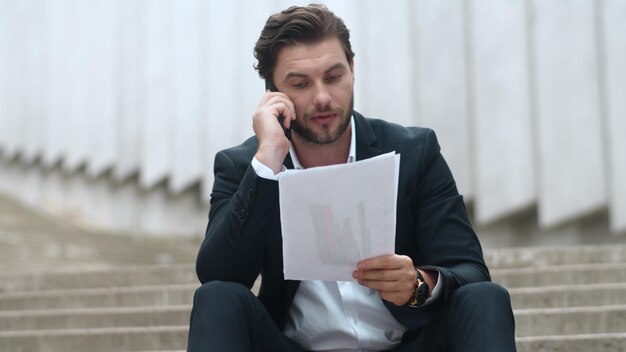 Photo businessman talking on smartphone in city man throwing documents on floor