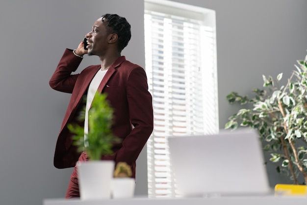 Businessman talks on phone in office smiles looks out window dressed in maroon suit