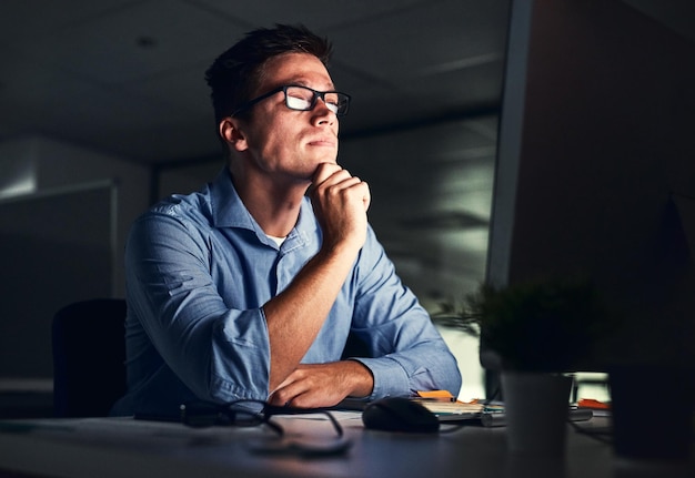 Photo businessman thinking of ideas in front of a computer while working late in an office at night hard working entrepreneur sending emails online research and reports trying to reach deadline overtime