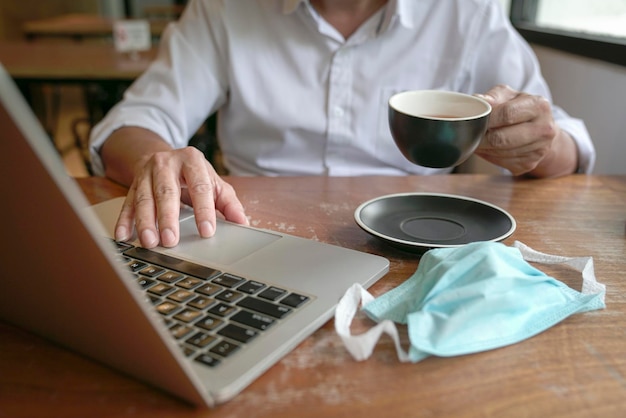 Businessman touching mouse pad on laptop and holding cup of tea with another hand