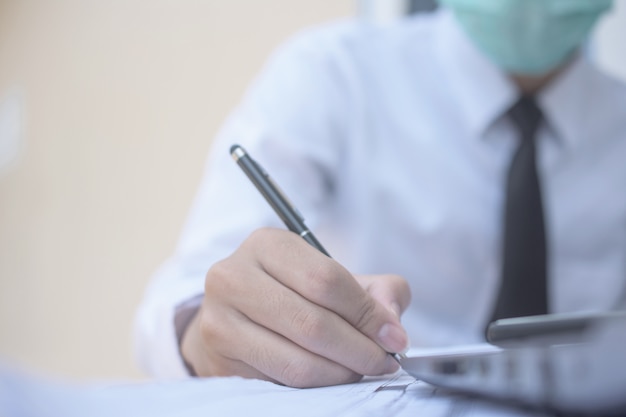 Бизнесмен использовать хирургическую маску и работать в офисе, а затем написать на деловой документ