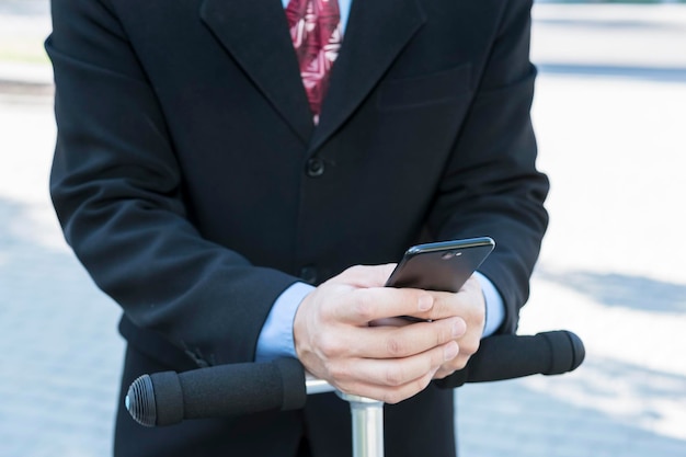 Businessman uses a smartphone, leaning on the steering wheel scooter, close-up