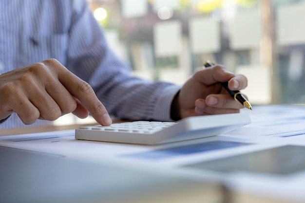 Businessman using a calculator to calculate numbers on a company's financial documents, he is analyzing historical financial data to plan how to grow the company. Financial concept.