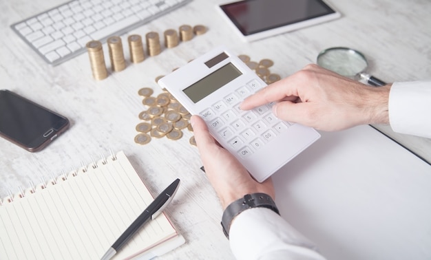 Businessman using calculator with coins on the desk.