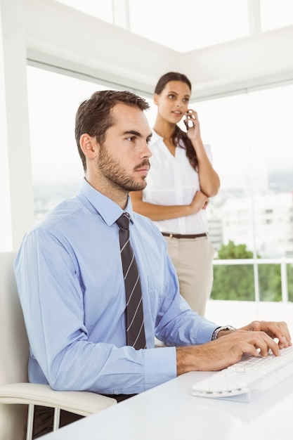 Businessman using computer while woman on call