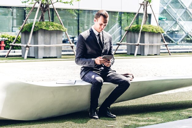 Businessman using digital tablet sitting against building