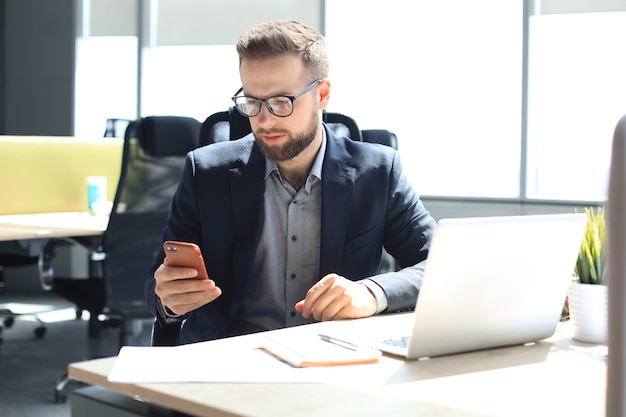 Uomo d'affari che utilizza il suo telefono cellulare in ufficio.