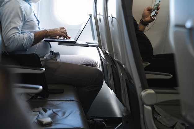 Foto uomo d'affari che utilizza laptop in aereo e passeggero in prima fila con il cellulare modalità volo dispositivo