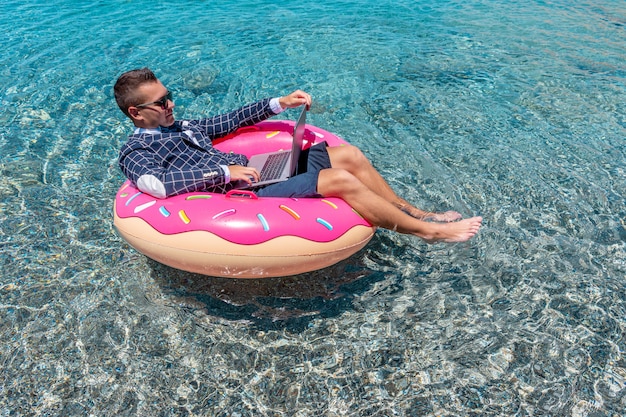 Businessman using laptop computer on an inflatable donut in the sea