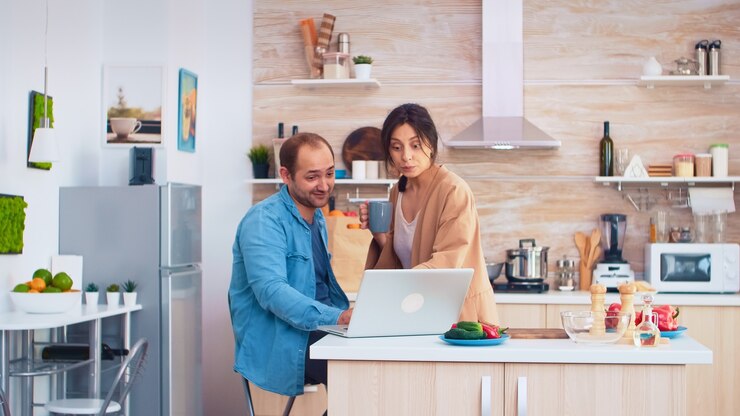 फोटो businessman using laptop in kitchen and wife is drinking a cup of coffee. husband and wife cooking recipe food. happy healthy together lifestyle. family searching for online meal. health fresh salad