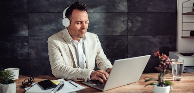 Uomo d'affari che per mezzo del computer portatile e ascoltando musica sulle cuffie