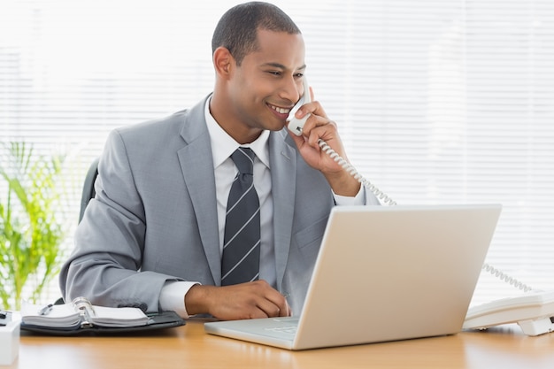 Businessman using laptop and phone at office desk