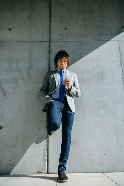 Businessman using mobile leaning on a concrete wall