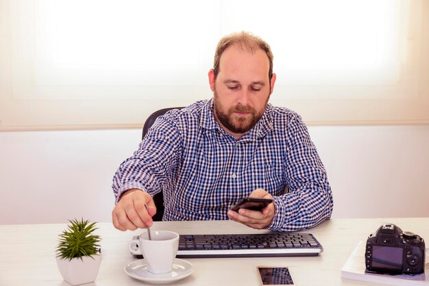 Businessman using phone while having coffee at desk in office