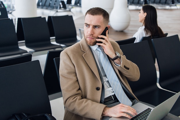 Uomo d'affari facendo uso dello smartphone dentro l'edificio per uffici o l'aeroporto.