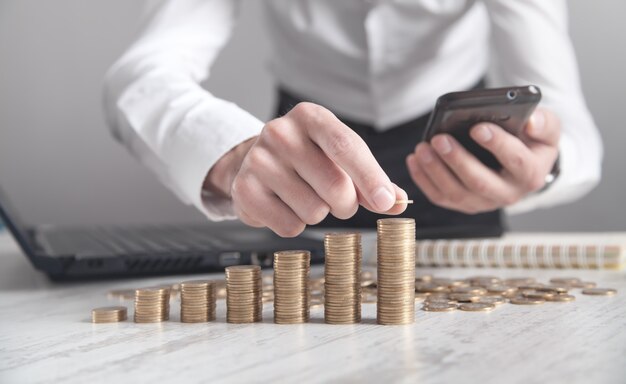 Businessman using smartphone and stacking coins on the desk.