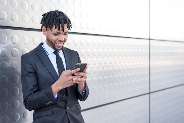 Businessman using smartphone at street silver wall