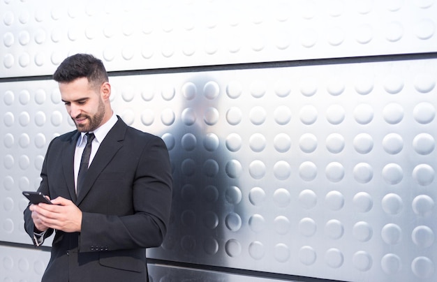 Businessman using smartphone at street silver wall