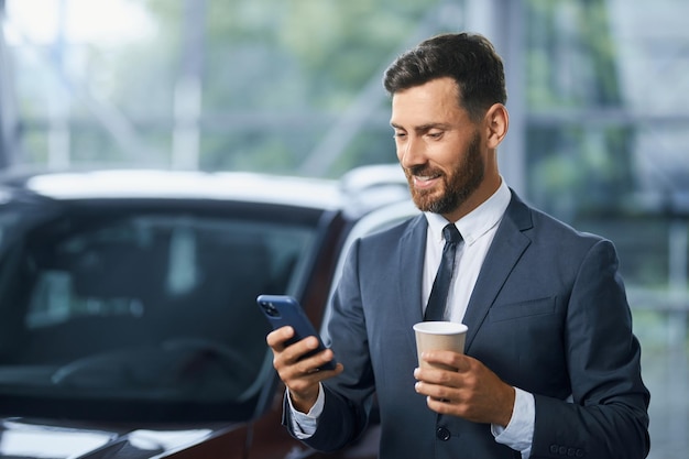 Uomo d'affari che utilizza smartphone durante l'acquisto di una nuova auto al salone