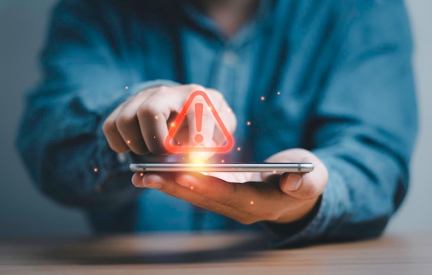 Businessman using smartphone with red triangle caution warning sign for notification error and maintenance support concept