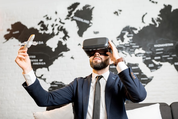 Uomo d'affari che utilizza occhiali per realtà virtuale seduti al chiuso con mappa del mondo sullo sfondo