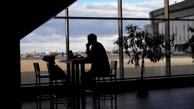 Businessman waiting for boarding at the airport and looking through panoramic windows silhouette of