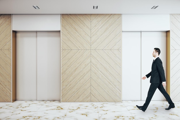 Businessman walking in office interior with two elevators