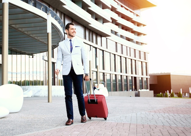 Фото Бизнесмен, идущий в вестибюль отеля. полнометражный портрет молодого руководителя с чемоданом.