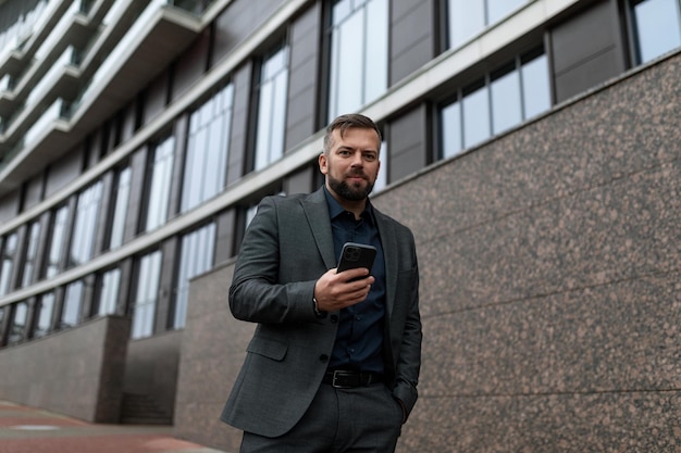 A businessman walks along the building on the street with a\
mobile phone in his hands