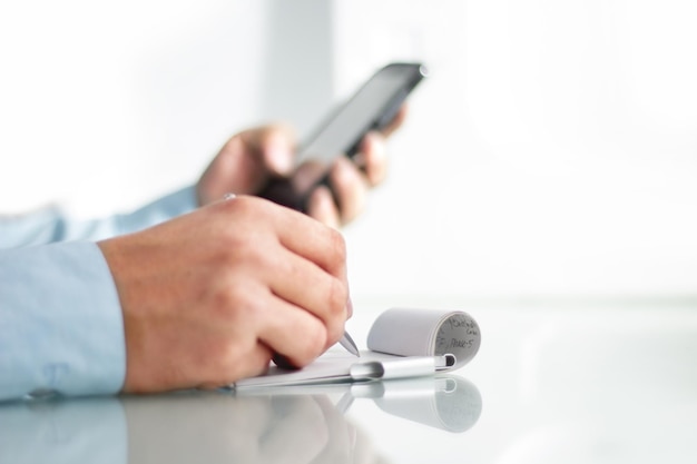 Businessman watching something on smartphone and writing something on diary