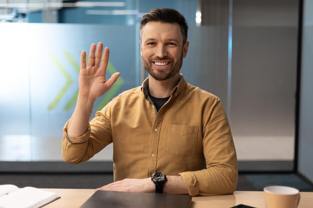 Businessman waving hand to camera having video call in office