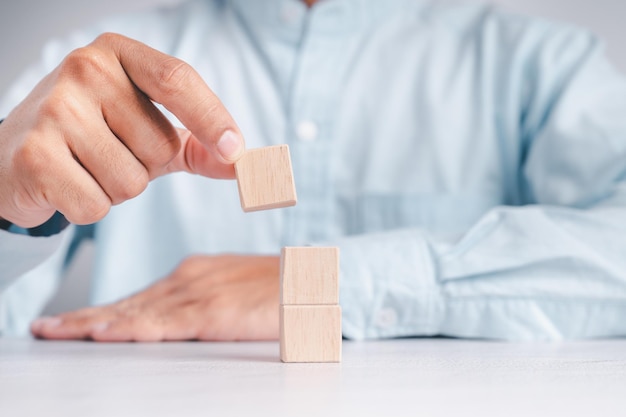 Businessman wearing a blue shirt arranging the empty wooden blocks with his hands Which is placed on a white wooden table Business strategy and action plan Copy space