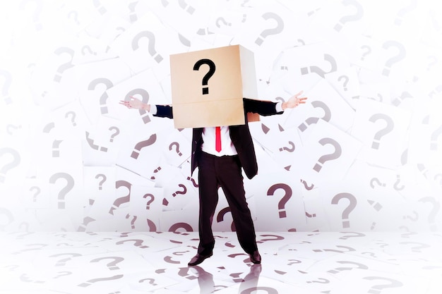 Businessman wearing carton box on head surrounded by question marks