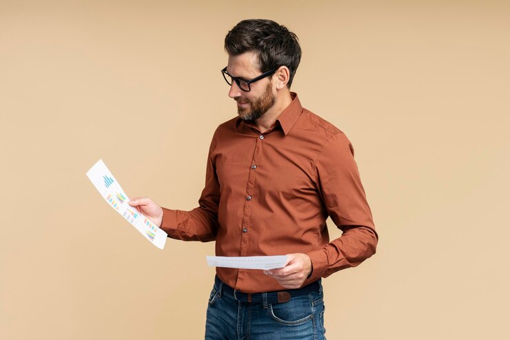 Photo businessman wearing eyeglasses holding documents reading contract isolated on beige background