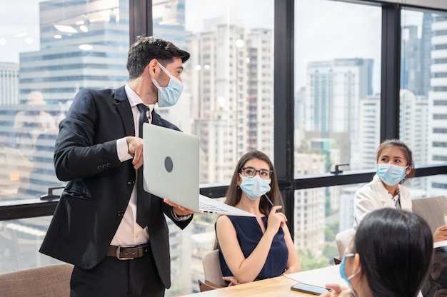 Businessman wearing face mask with presentation of business plan on laptop