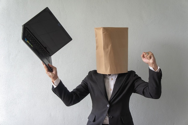 Photo businessman wearing paper bag over face while using laptop against wall