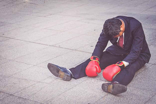 Businessman wearing red boxing glove sitting on the floor but feeling stress about work. 