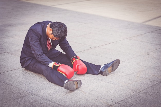 Foto uomo d'affari che indossa il guantone da pugile rosso seduto sul pavimento ma sentirsi stress sul lavoro.