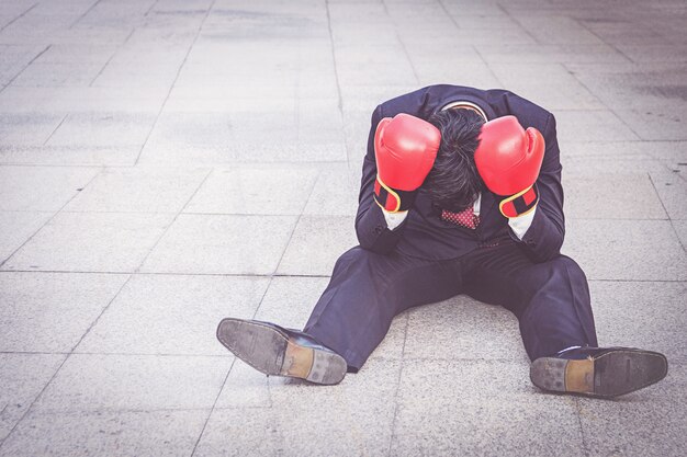 Businessman wearing red boxing glove sitting on the floor but feeling stress about work. 