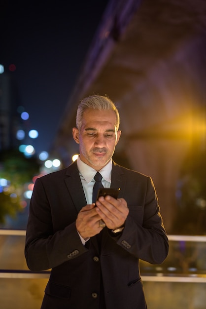 Businessman wearing suit in city at night while using mobile phone