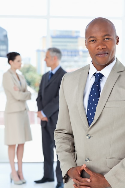 Businessman wearing a suit and crossing his hands with his team behind him