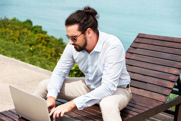 Uomo d'affari che indossa un abito sulla sedia a sdraio digitando laptop sulla spiaggia